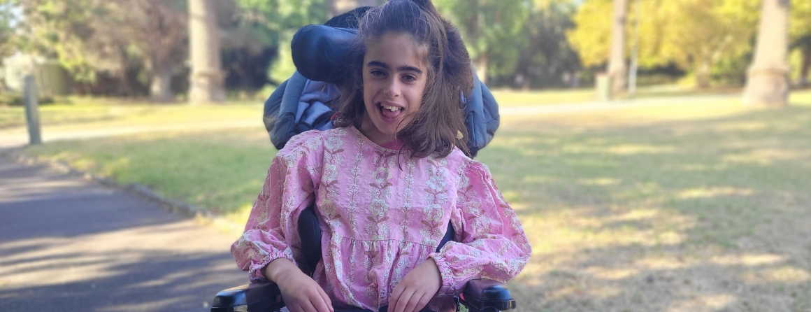 Gitty smiling whilst sitting in her wheelchair in the park